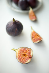 One whole fig and the other sliced lie on a white table.