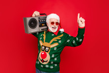 Photo Of Elderly Funny Santa Man Hold Vintage Tape Recorder Chilling At Youngster Party Long Waited Guest Wear Specs X-mas Ugly Ornament Sweater Cap Isolated Red Background