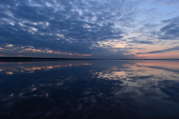 Wall Mural - Cloudy blue sky at dusk reflection on a clean surface of the water in the calm weather of an autumn evening