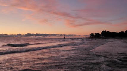 Wall Mural - Gorgeous panoramic landscape view of a colorful blue pink and purple sunrise over the water of Lake Michigan as waves gently roll in to the shoreline with clouds on the horizon.