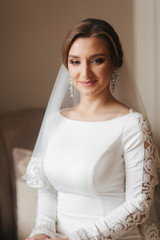 Wall Mural - Close up portrait of beautiful bride standing by the window at home. Charming bride in white wedding dress