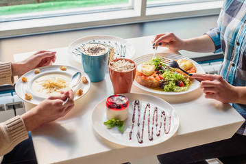 Healthy breakfast. Brunch Toasts with salmon, poached egg, fresh salad and plate with mashed soup on white table in restaurant. Girls have breakfast in cafe. Close-up