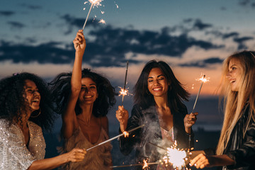 Wall Mural - Four happy women celebrating at sunset with sparklers