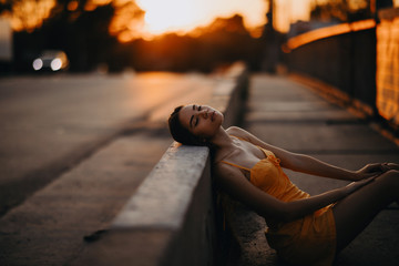 Wall Mural - A woman sits on the sidewalk in a yellow dress at sunset.