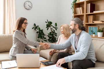 Casual bearded man shaking hand of young female real estate agent over desk