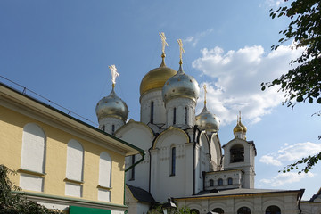 Golden domes with crosses of an orthodox temple on the background of bright blue sky. Snow-white facade. Christian faith.