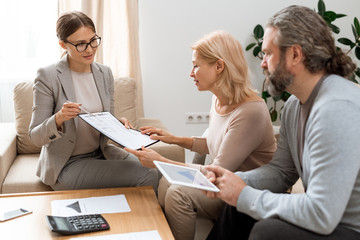 Canvas Print - Young real estate agent pointing at document while consulting mature clients