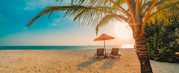 Beautiful tropical sunset scenery, two sun beds, loungers, umbrella under palm tree. White sand, sea view with horizon, colorful twilight sky, calmness and relaxation. Inspirational beach resort hotel