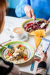 © Kirill - Woman in restaurant eats pancakes with red caviar and holds the phone in her hand. Business lunch. Maslenitsa. Close-up. Space