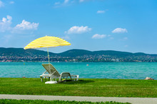 Stylish Lounger Plastic Sunbed With Yellow Stripes Sunshade Beach Umbrella On The Green Grass On Beach At Summer Under Open Sky. Sunbed Intended For Cold Shadow On Convenient Lounger At Lake Balaton
