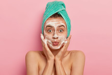 Image Of Attractive Female Washes Face With Foam, Massages Cheeks, Looks Surprisingly At Herself, Wears Wrapped Towel On Head, Removes Dirt, Feels Freshness After Taking Shower, Models Indoor