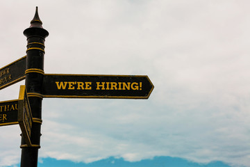 Conceptual hand writing showing We Are Re Hiring. Concept meaning process of reviewing applications and finding candidates Road sign on the crossroads with blue cloudy sky in the background