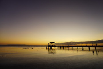 Wall Mural - Two people watch a sunset from a pier leading into a lagoon on the island of Fakarava in French Polynesia