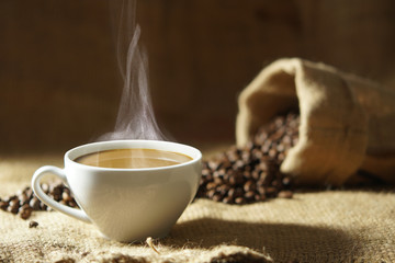 white coffee cup with hot steam smoke and roasted coffee beans around