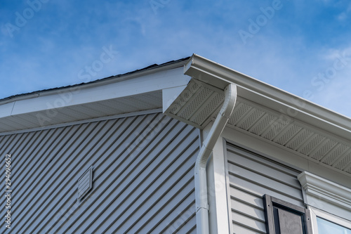 Gable with grey horizontal vinyl siding, white frame gutter guard system, fascia, drip edge, soffit, on a pitched roof attic at a luxury American single family home neighborhood USA