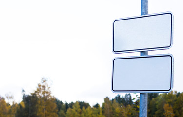 Two empty white road blank signs on a pillar outdoor on parking sign with autumn forest on background. Place for text. Mock up.