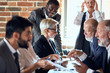 © alfa27 - Group of businessmen wear suits sit at table in office and discuss new project, smile. caucasian blond woman and african man stand, behind open window. Camera focused on man and woman speak