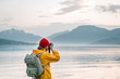 Traveler photographer wearing yellow raincoat taking photo by professional camera of fantastic scandinavia nature. Man tourist tourist travels to beautiful mountain and fjord places