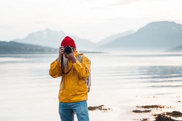 Hipster traveler photographer takes a photo beautiful nordic landscape on professional camera. Man tourist with backpack shoots a photo scandinavia nature