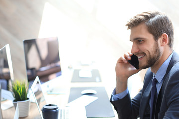 Modern businessman analyzing data using computer and talking on the phone while sitting in the office.