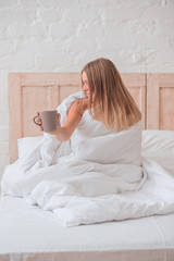 Wall Mural - Beautiful girl sitting in her bed dreaming and drinking morning drink, bedroom in loft style