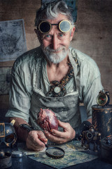 Man in steampunk glasses with gray hair and beard holding human heart. Fantasy, fairy tale. Inventor in  post apocaliptic world