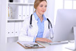 © rogerphoto - Young woman doctor at work in hospital looking at desktop pc monitor. Physician controls medication history records and exam results. Medicine and healthcare concept