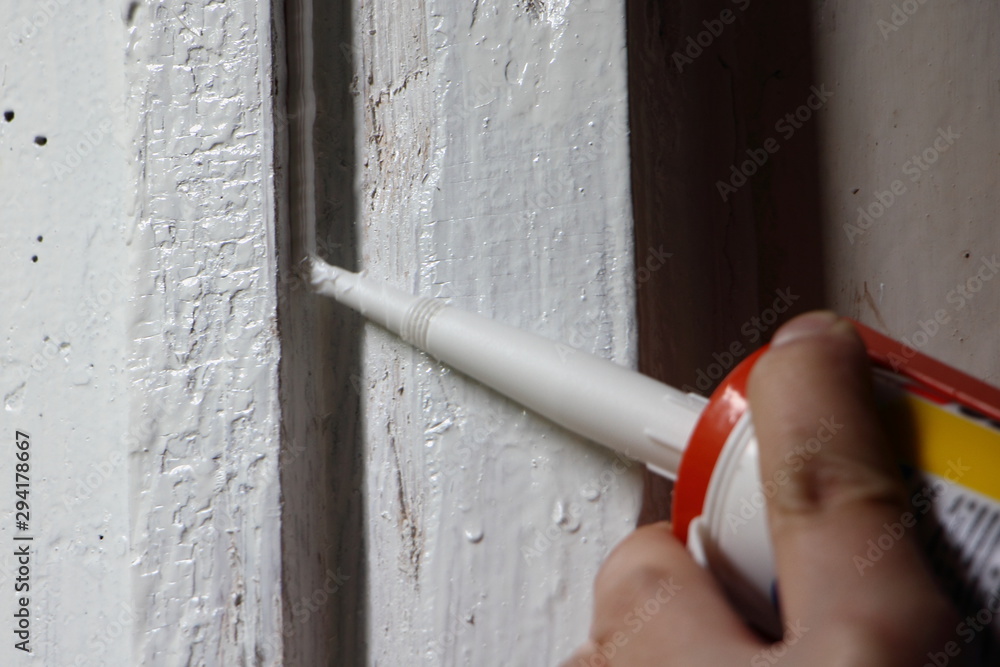 Application of white silicone sealant from a gun to an old painted vertical wooden surface - obrazy, fototapety, plakaty 