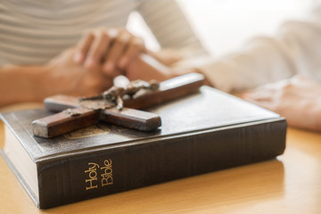 Wall Mural - Christian woman praying with hands together on holy bible and wooden cross. Woman pray for god blessing to wishing have a better life and believe in goodness.