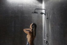 Woman Taking Shower In Dark Modern Bathroom Interior
