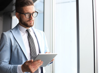 Wall Mural - Modern business man in formalwear using digital tablet while standing near window in the office