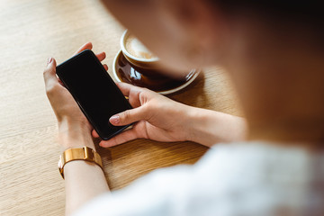 Close up of woman's hands holding cell telephone with blank copy space scree for your advertising text message or promotional content, hipster girl watching video on mobile phone during coffee break