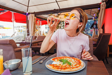 Wall Mural - Young girl eating delicious pizza with cheese and greens in pizzeria