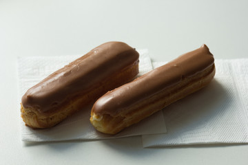 Two eclair with chocolate topping on the white napkins on white background