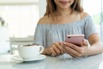 Wall Mural - Women using mobile phone with a cup of coffee on marble desk in cafe.