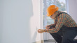 © procinemastock - Man wearing brown shirt and dungarees working on electrical wall socket wires using screwdriver, electrician concept.