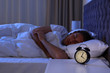 Alarm clock on nightstand near sleeping young man. Bedtime