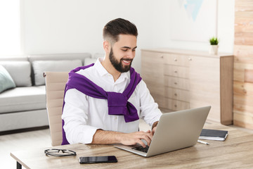 Wall Mural - Handsome young man working with laptop at table in home office