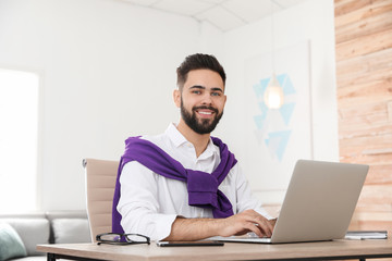 Wall Mural - Handsome young man working with laptop at table in home office