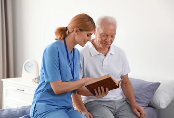 Poster - Nurse reading book to elderly man indoors. Medical assistance