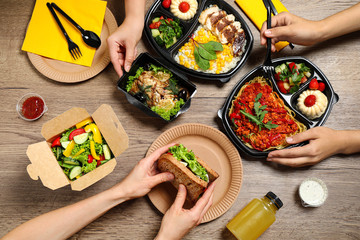 People eating healthy meals at wooden table, top view. Food delivery