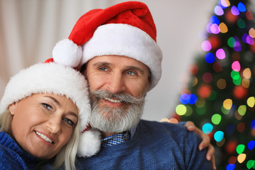 Wall Mural - Happy mature couple in Santa hats celebrating Christmas at home