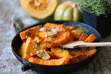 Baked pumpkin slices in a pan with herbs and garlic. Autumn lunch. Vegan food. Healthy snack.