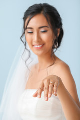 Poster - Beautiful young Asian bride showing her wedding ring against color background