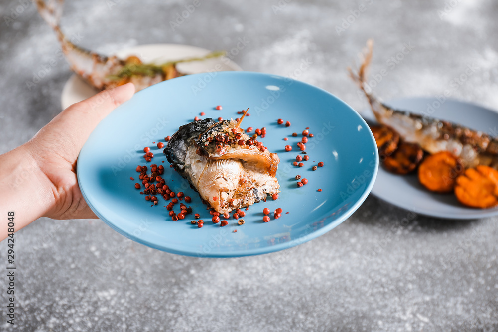 Female hand with prepared mackerel fish on plate, closeup