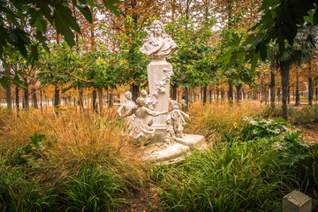 Alley of the Jardin des Tuileries covered with orange autumn leaves, statue in the Tuileries garden in Paris France on a beautiful Fall day