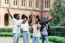 Four Happy African Students Best Friends Standing Near University With Raised Hands