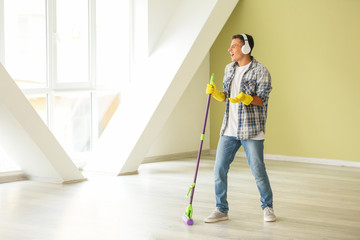 Poster - Young man listening to music and singing while cleaning his flat