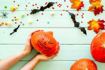 Make pumpkin decoration for Halloween. Pumpkin in hands on green wooden background top view copy space