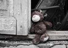 Little Teddy Bear Sits On The Doorstep Near An Old Door With Cracked Paint